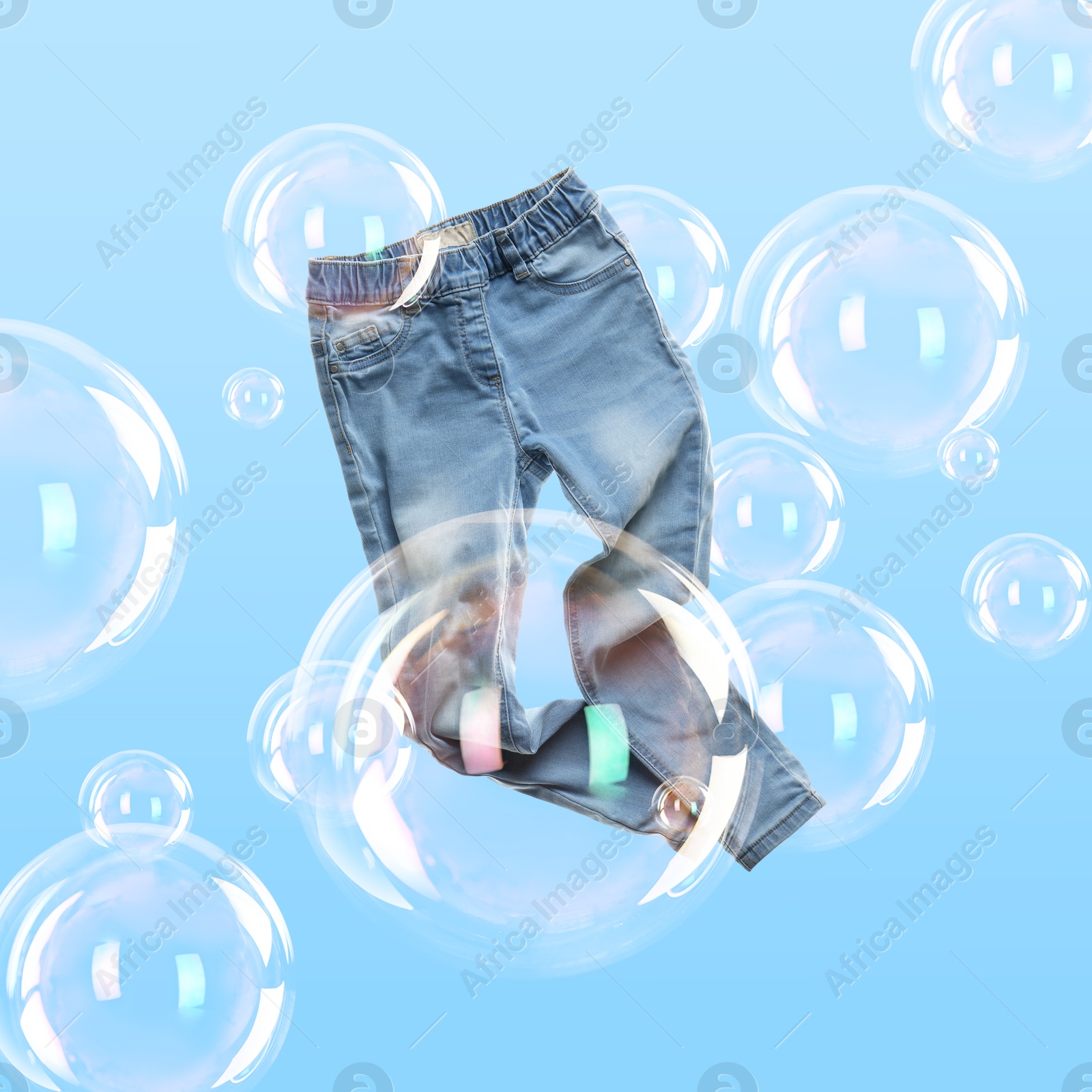 Image of Jeans flying among soap bubbles on light blue background. Laundry day