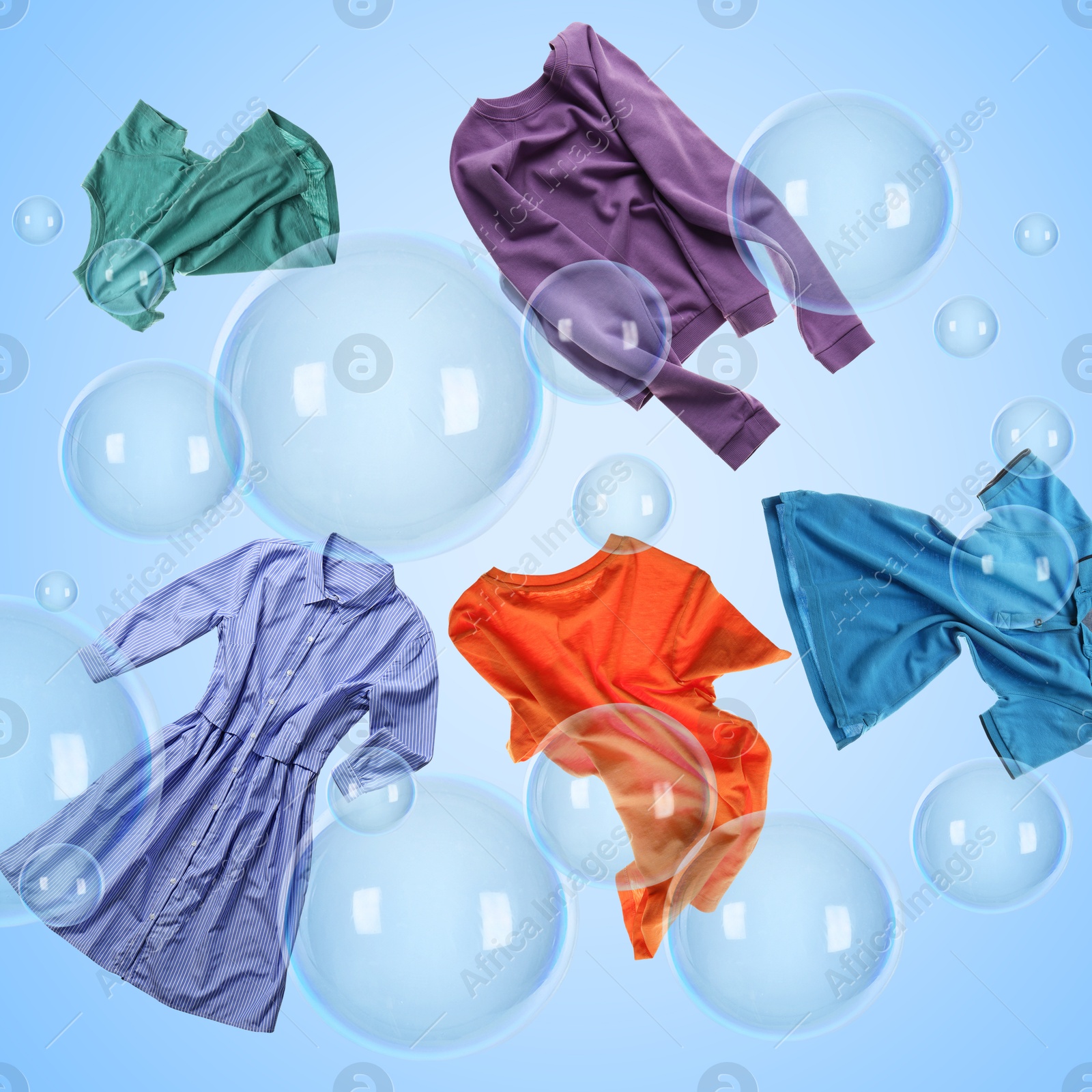 Image of Different clothes flying among soap bubbles on light blue background. Laundry day