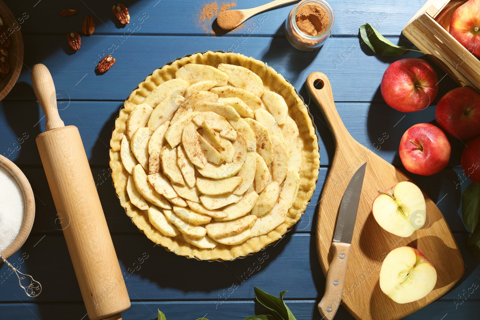 Photo of Uncooked homemade apple pie and ingredients on blue wooden table, flat lay