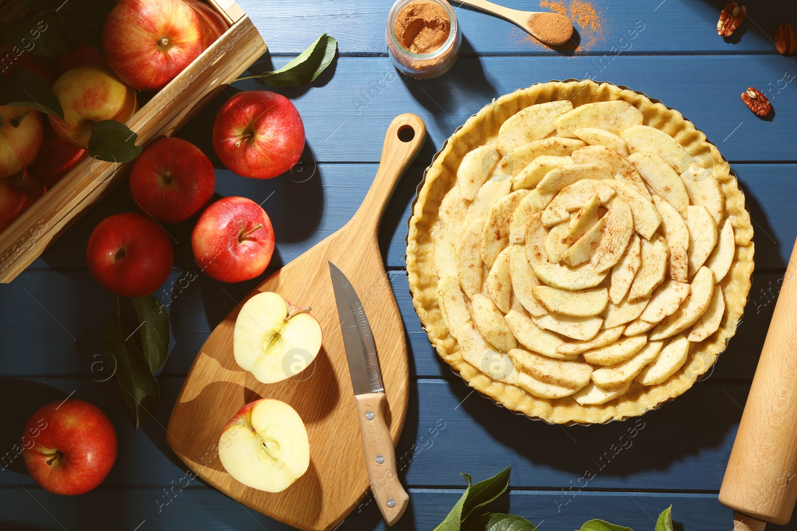 Photo of Uncooked homemade apple pie and ingredients on blue wooden table, flat lay