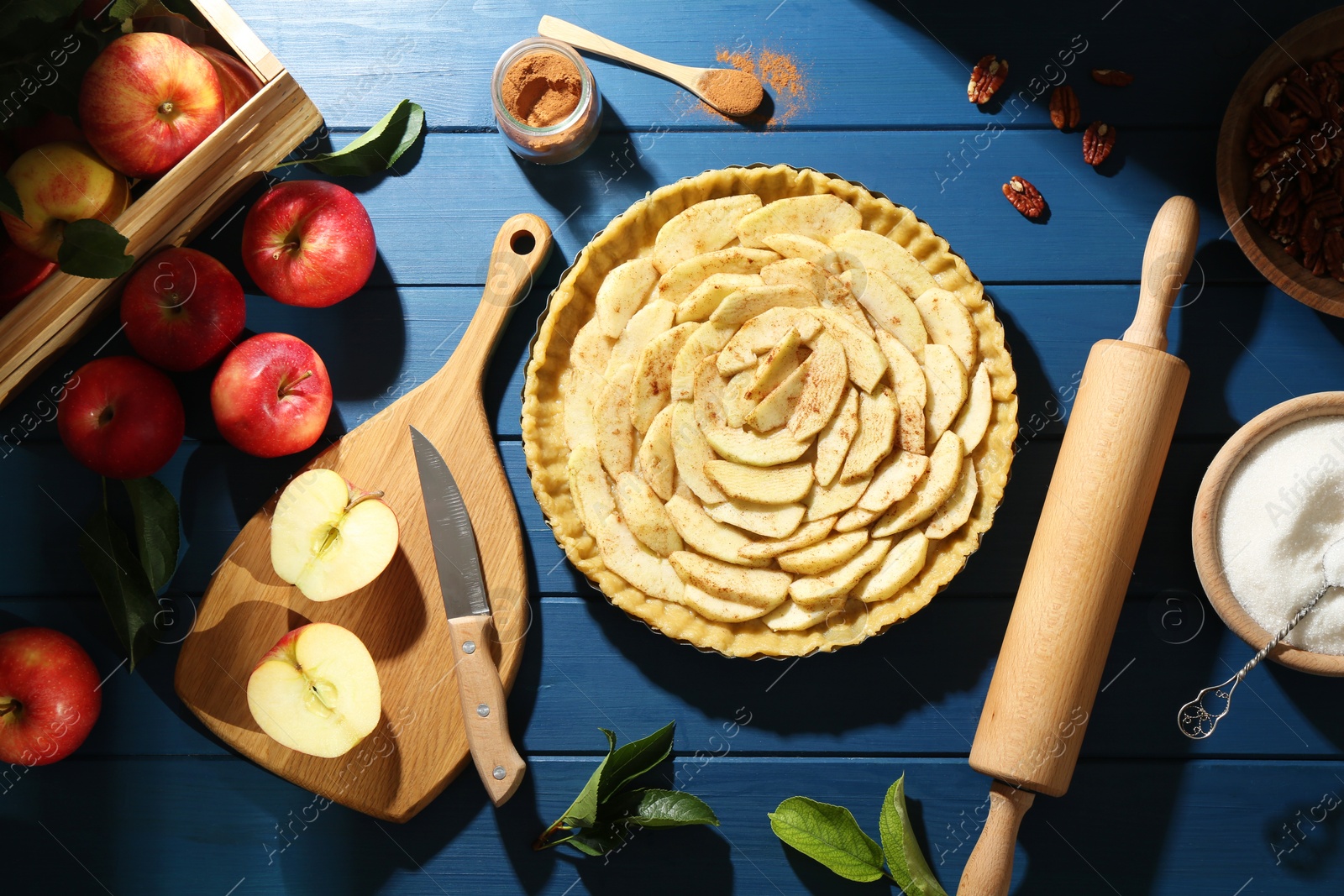 Photo of Uncooked homemade apple pie and ingredients on blue wooden table, flat lay