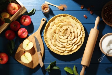 Photo of Uncooked homemade apple pie and ingredients on blue wooden table, flat lay