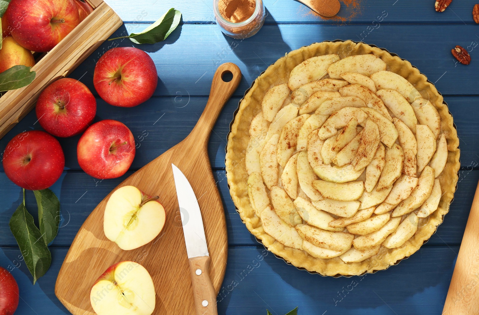 Photo of Uncooked homemade apple pie and ingredients on blue wooden table, flat lay