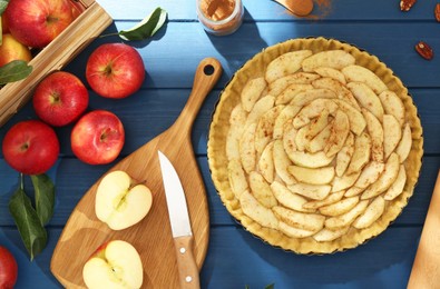 Photo of Uncooked homemade apple pie and ingredients on blue wooden table, flat lay