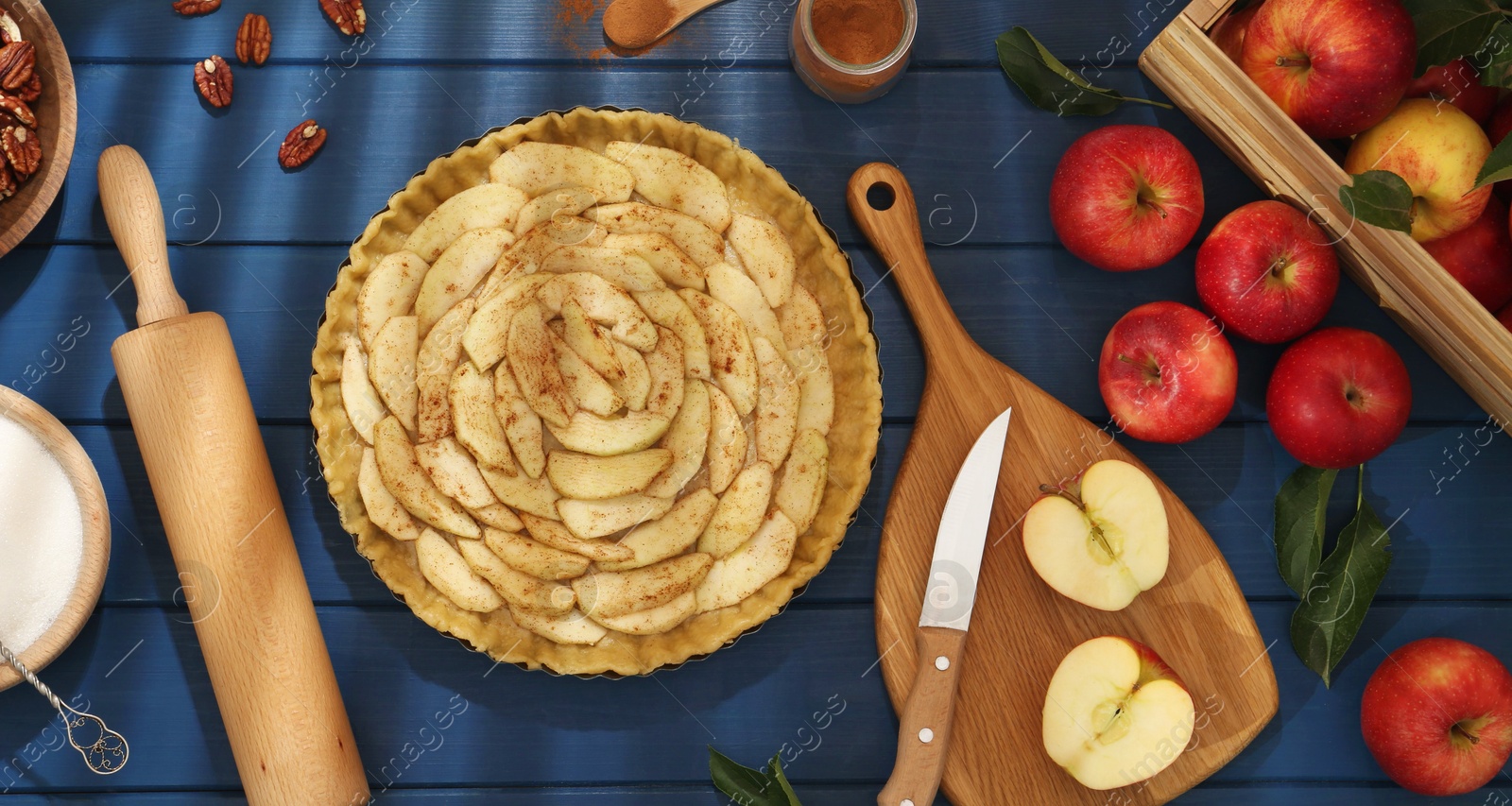 Photo of Uncooked homemade apple pie and ingredients on blue wooden table, flat lay