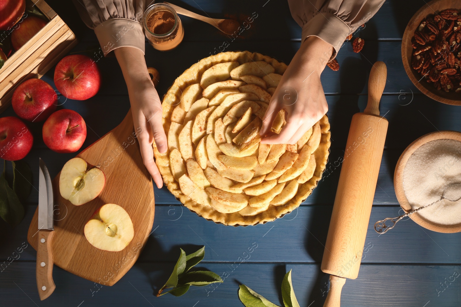 Photo of Woman making homemade apple pie and ingredients on blue wooden table, top view