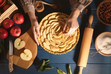 Photo of Woman making homemade apple pie and ingredients on blue wooden table, top view