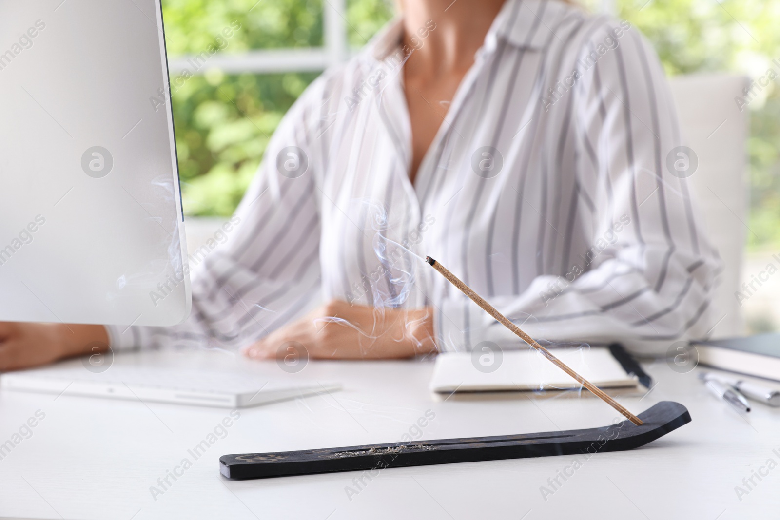 Photo of Woman working with computer at table while incense stick smoldering in holder indoors, selective focus