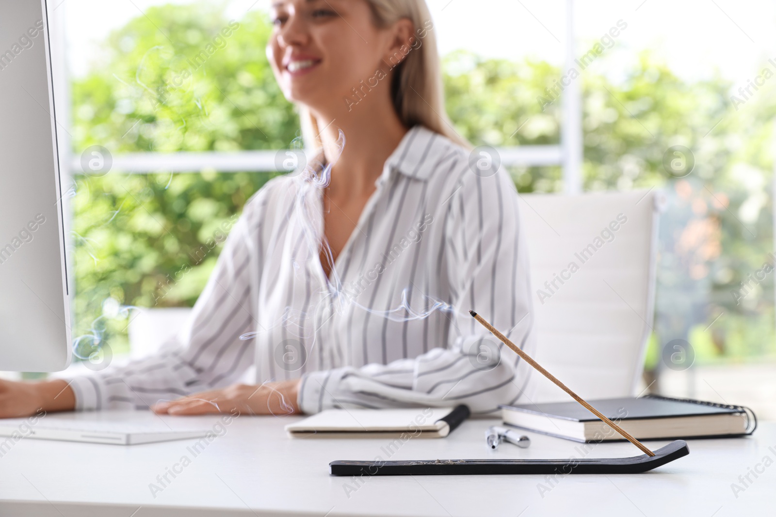 Photo of Woman working with computer at table while incense stick smoldering in holder indoors, selective focus