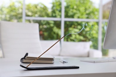 Photo of Incense stick smoldering in holder on white table in office