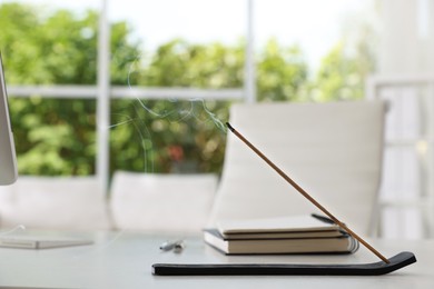 Photo of Incense stick smoldering in holder on white table in office, space for text