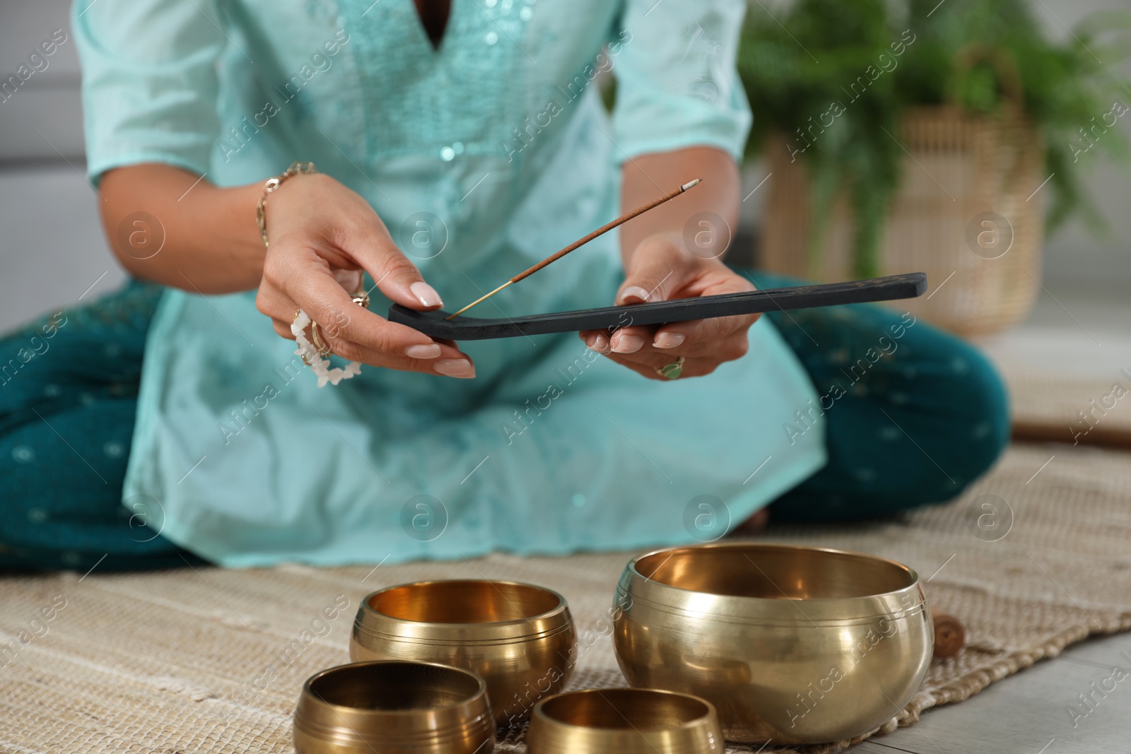 Photo of Woman with incense stick and tibetan singing bowls indoors, closeup