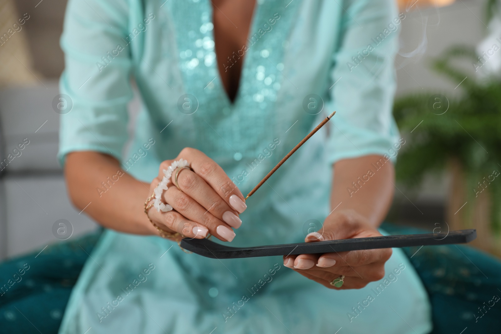 Photo of Young woman with incense stick smoldering in holder indoors, closeup