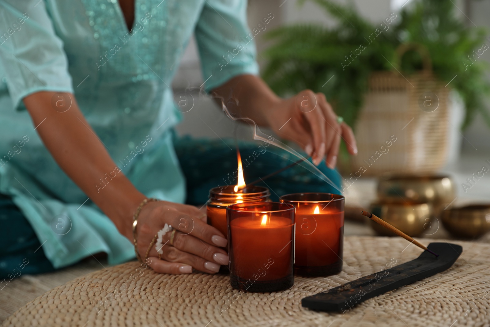 Photo of Woman lighting incense sticks with burning candles indoors, closeup