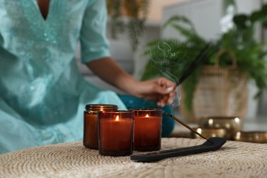 Photo of Woman with incense sticks and burning candles indoors, selective focus