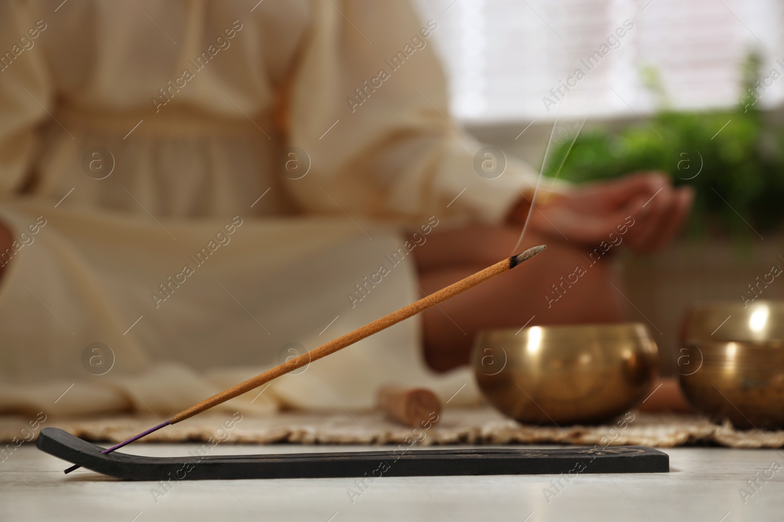 Photo of Incense stick smoldering in holder on floor indoors, selective focus