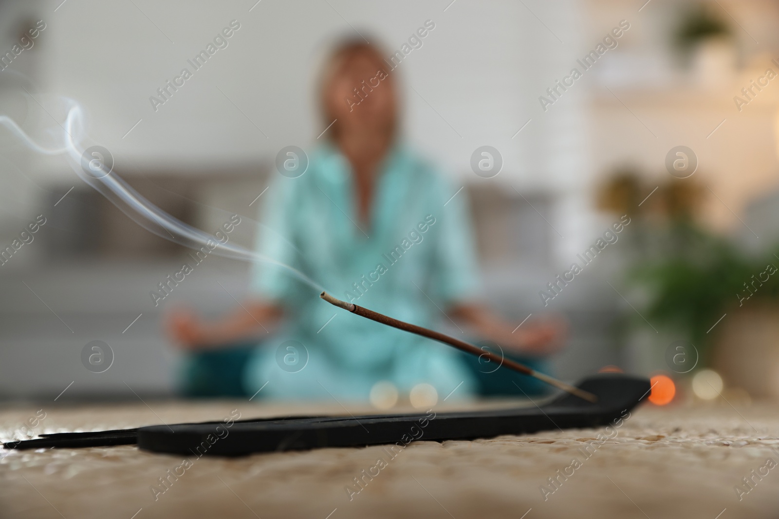 Photo of Incense stick smoldering in holder on mat indoors, selective focus