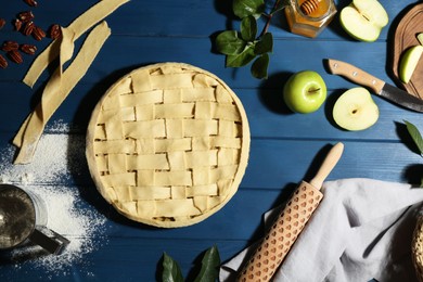 Photo of Uncooked homemade apple pie and ingredients on blue wooden table, flat lay