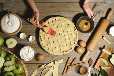 Photo of Woman making homemade apple pie and ingredients on wooden table, top view