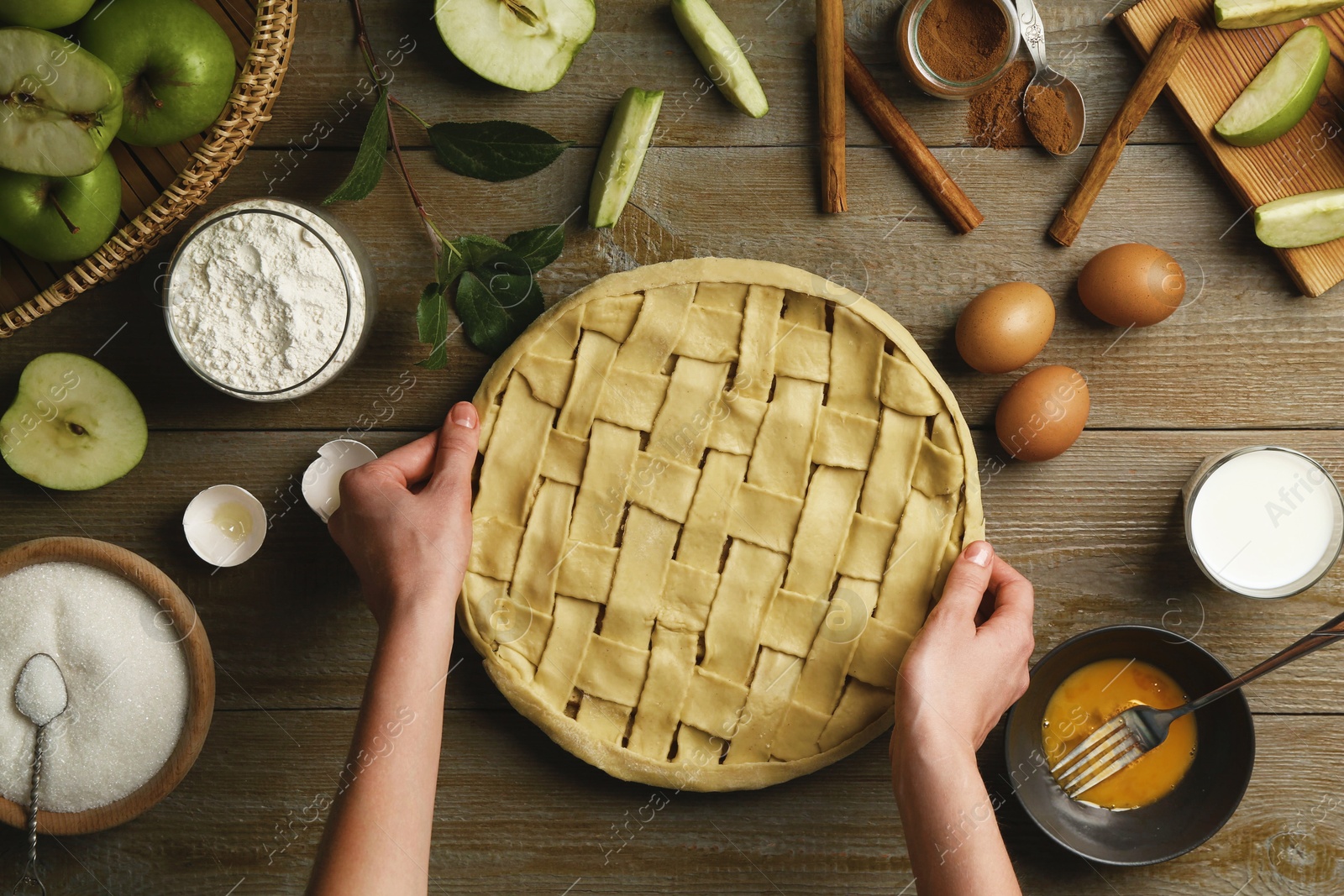 Photo of Woman making homemade apple pie and ingredients on wooden table, top view