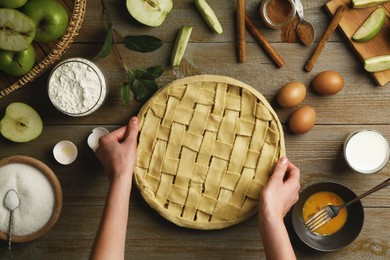 Photo of Woman making homemade apple pie and ingredients on wooden table, top view