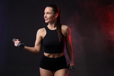 Photo of Woman exercising with dumbbells in smoke on dark background