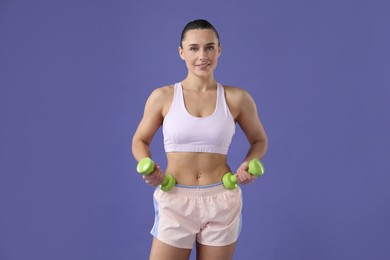 Photo of Woman exercising with dumbbells on purple background