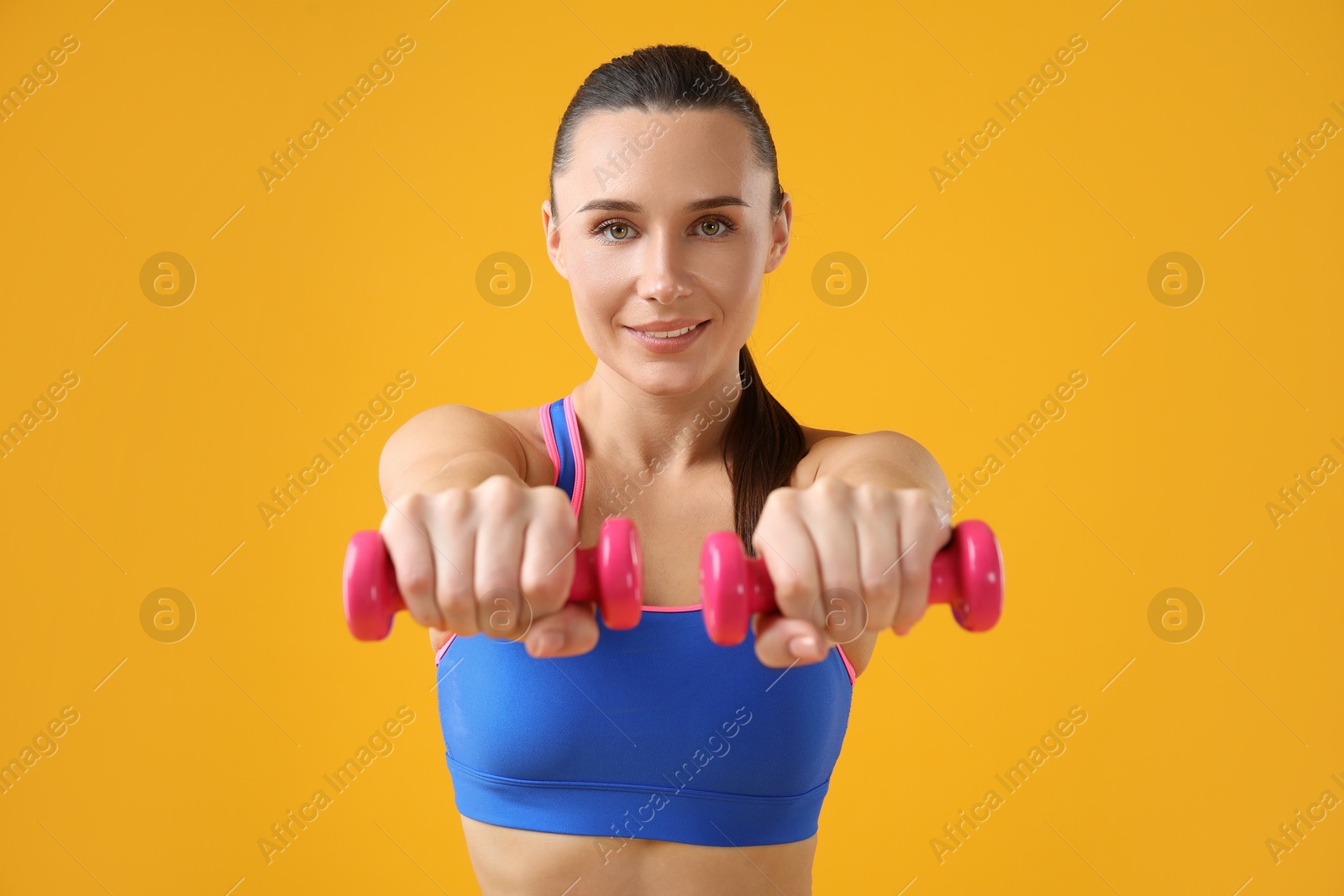 Photo of Woman exercising with dumbbells on orange background