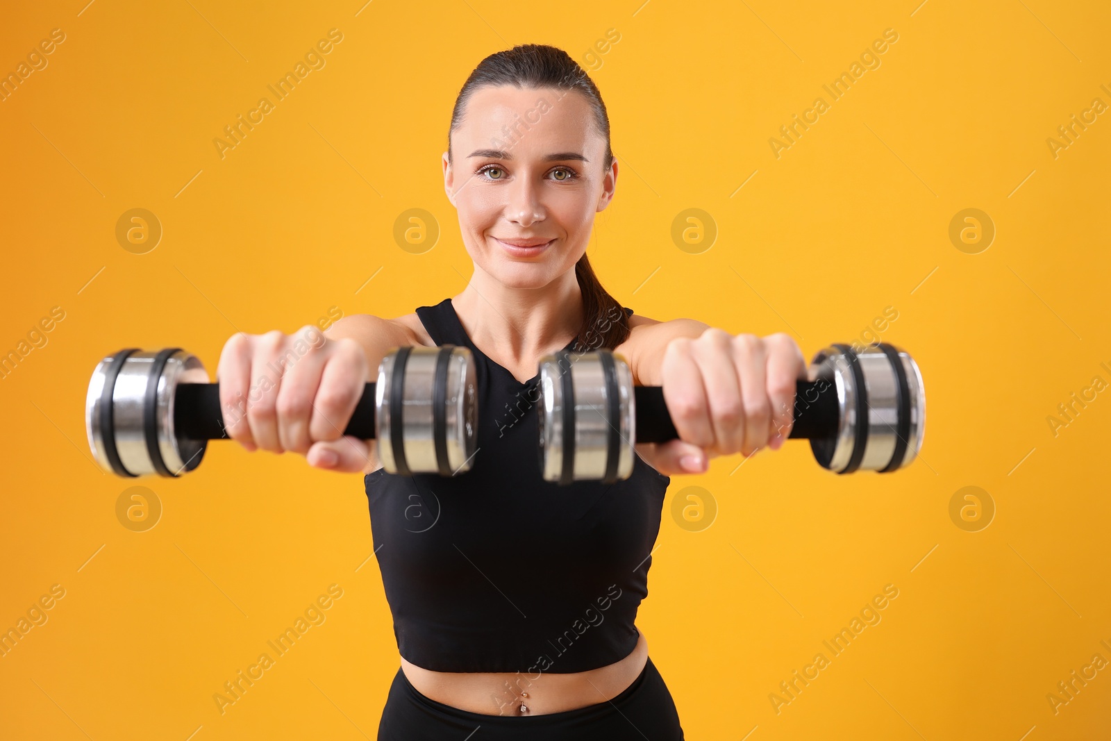 Photo of Woman exercising with dumbbells on orange background