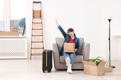 Happy woman with moving boxes and suitcase in new apartment. Housewarming party