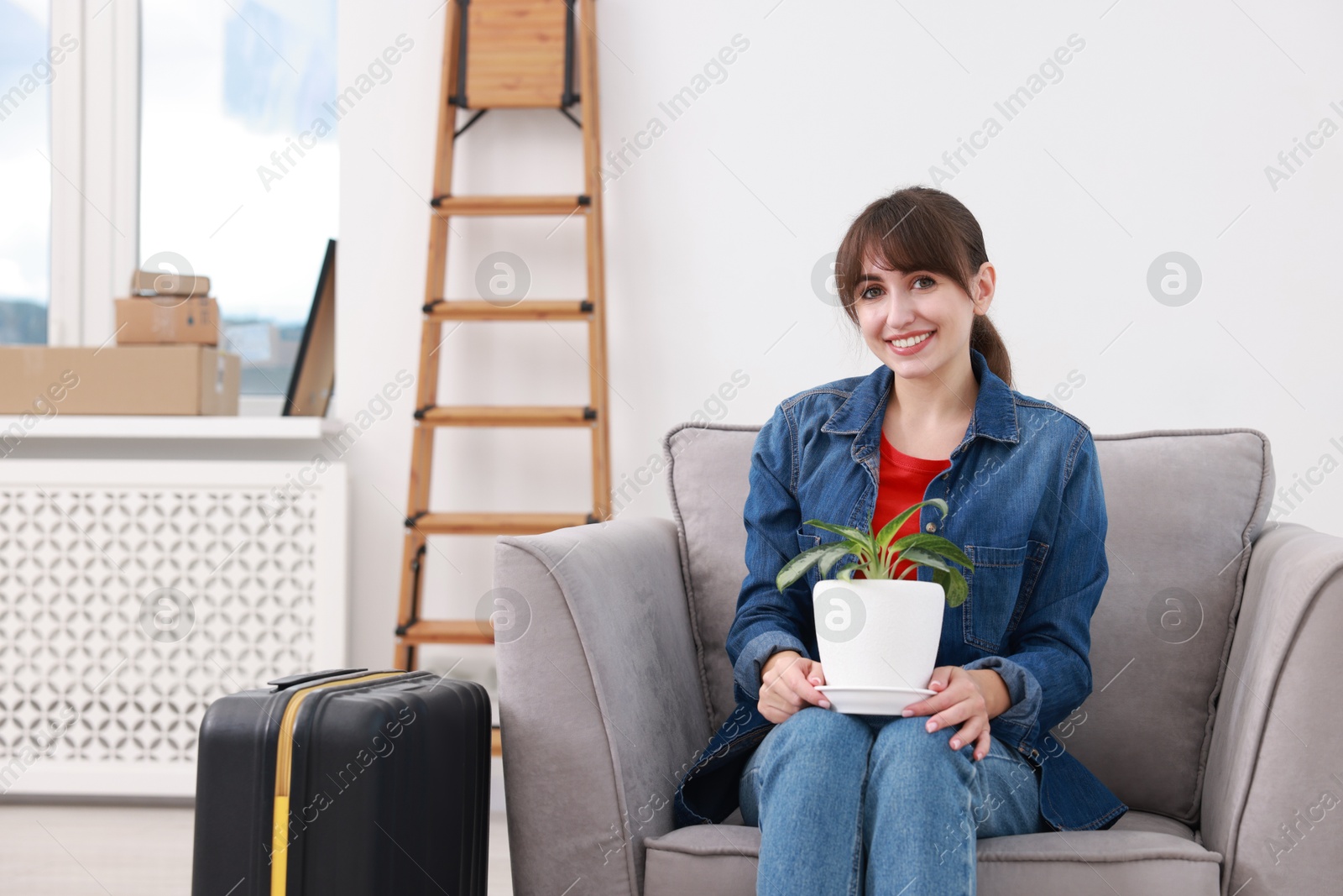 Photo of Happy woman with houseplant and suitcase in new apartment. Housewarming party