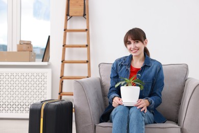 Photo of Happy woman with houseplant and suitcase in new apartment. Housewarming party