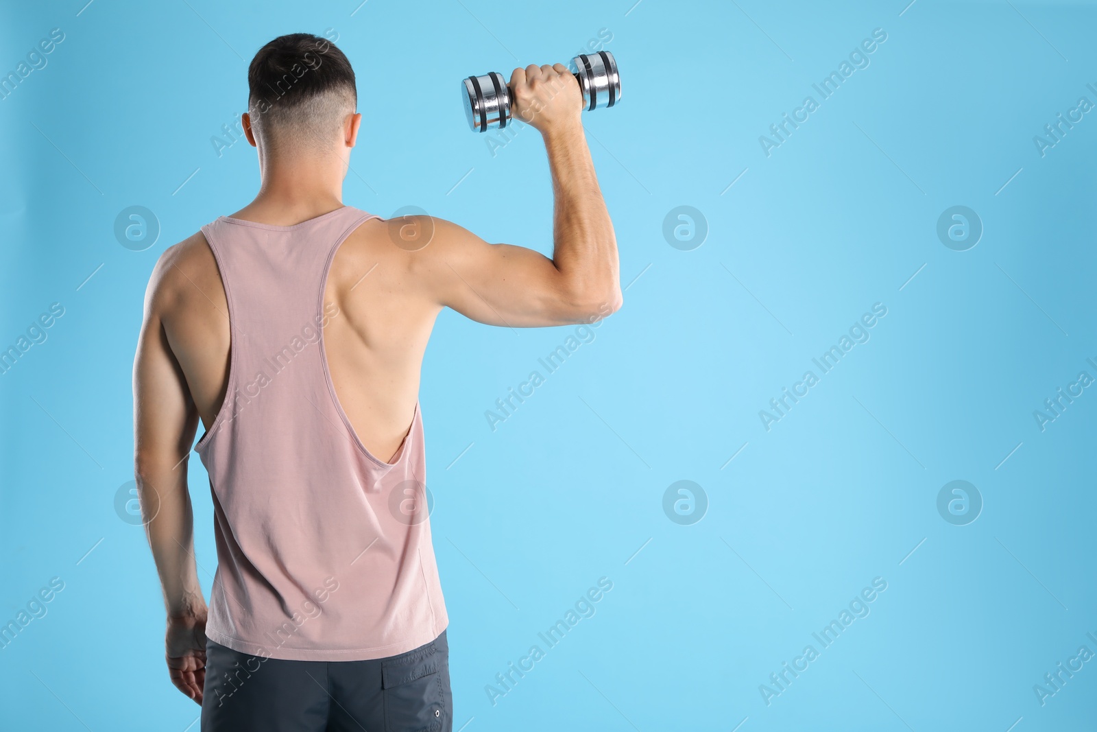 Photo of Man exercising with dumbbell on light blue background, back view. Space for text