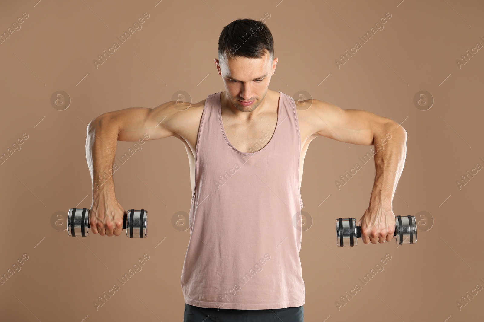 Photo of Man exercising with dumbbells on light brown background