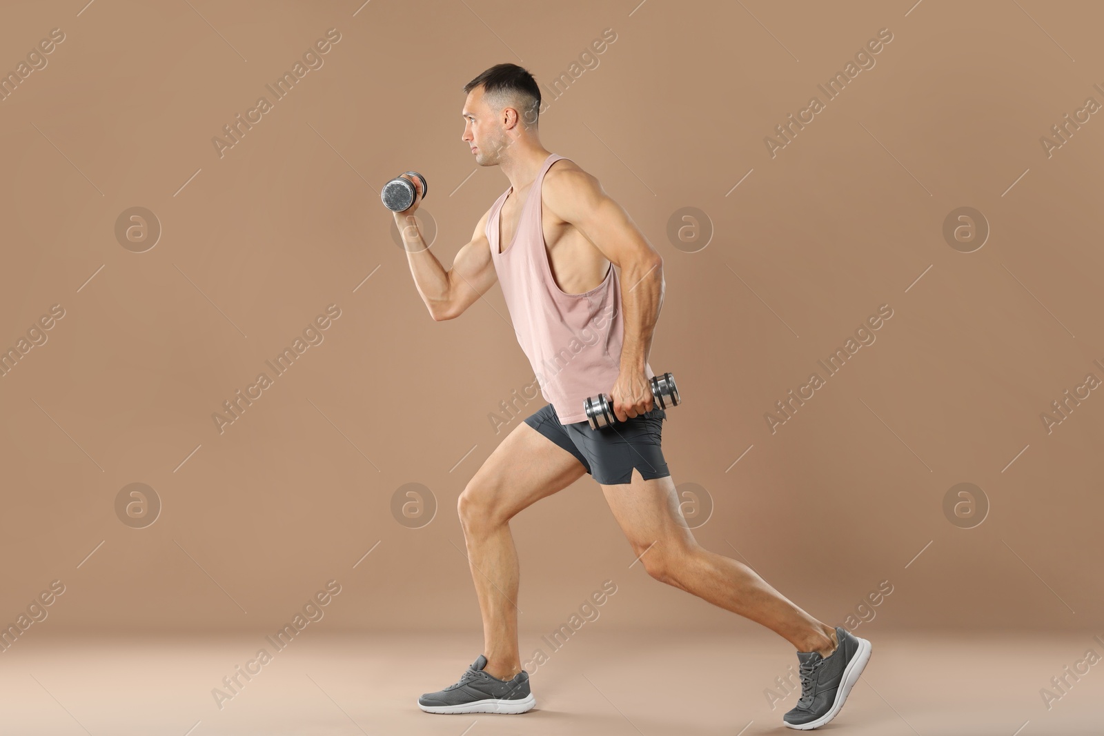 Photo of Man exercising with dumbbells on light brown background