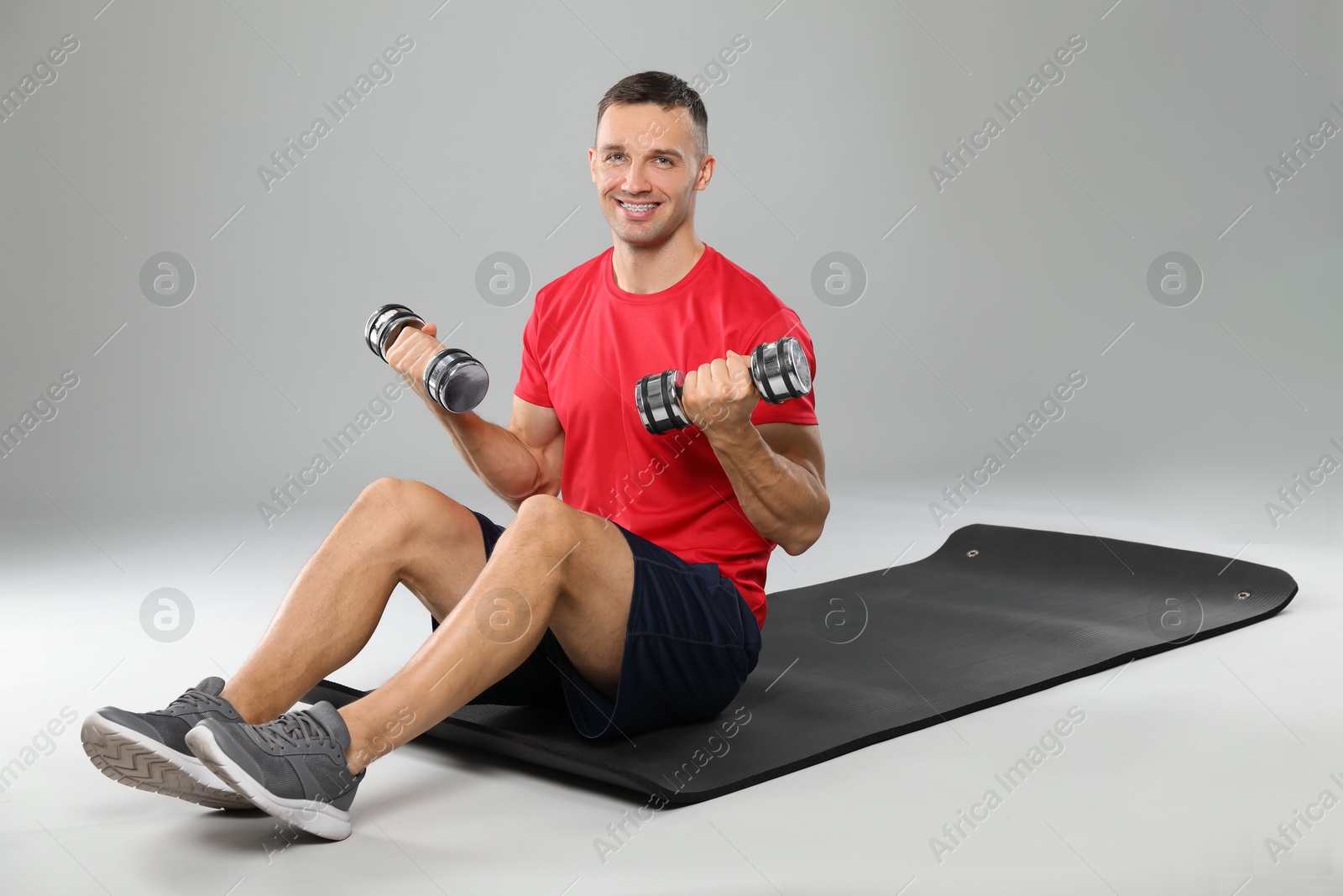 Photo of Man exercising with dumbbells on grey background