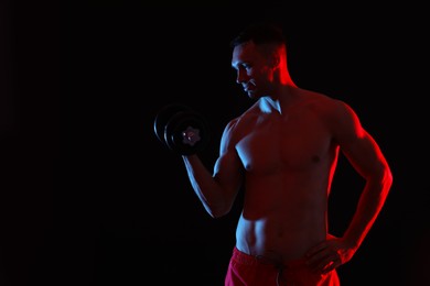 Photo of Man exercising with dumbbell in red light on black background. Space for text