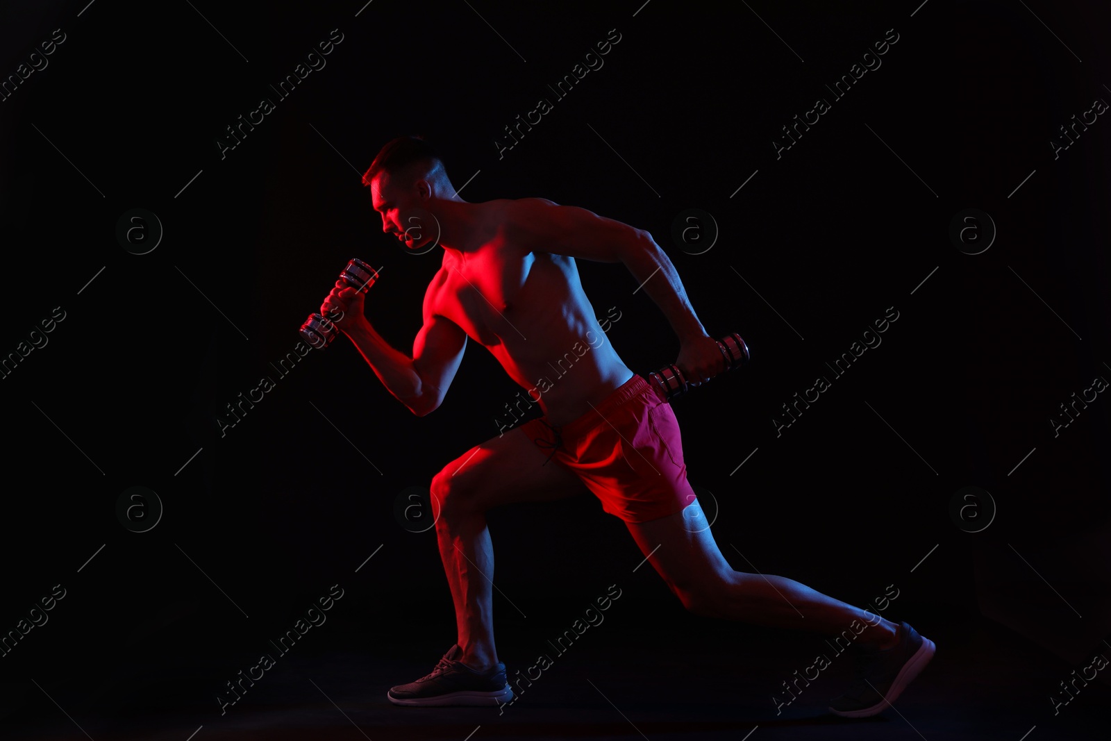 Photo of Man exercising with dumbbells in red light on black background