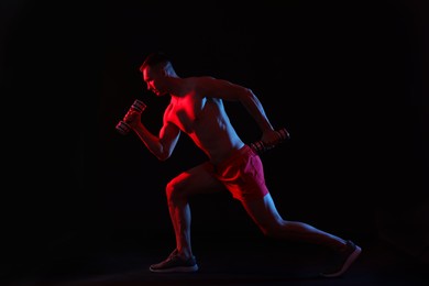 Photo of Man exercising with dumbbells in red light on black background