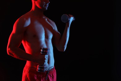 Photo of Man exercising with dumbbells in red light on black background, closeup. Space for text