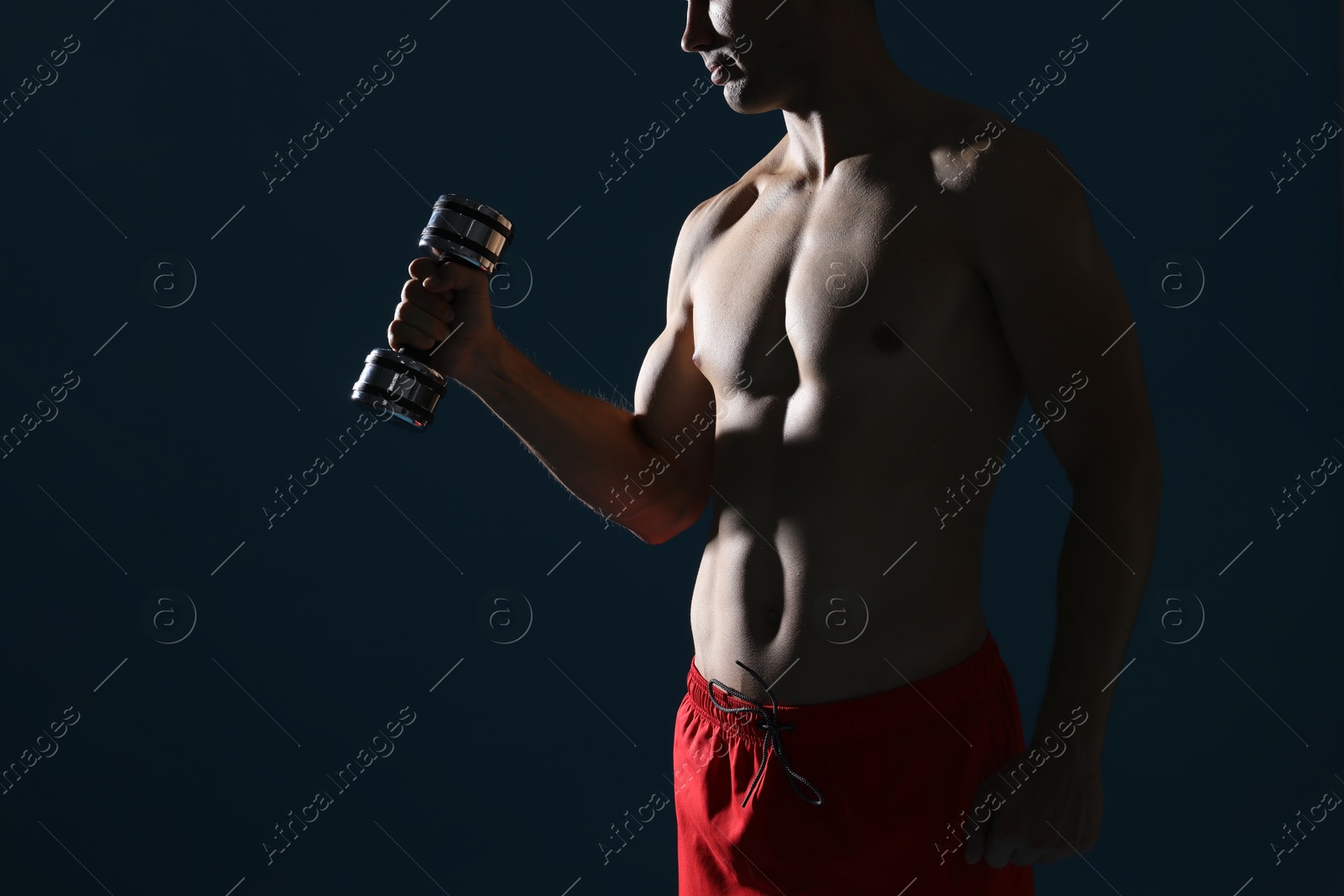 Photo of Man exercising with dumbbell on dark blue background, closeup