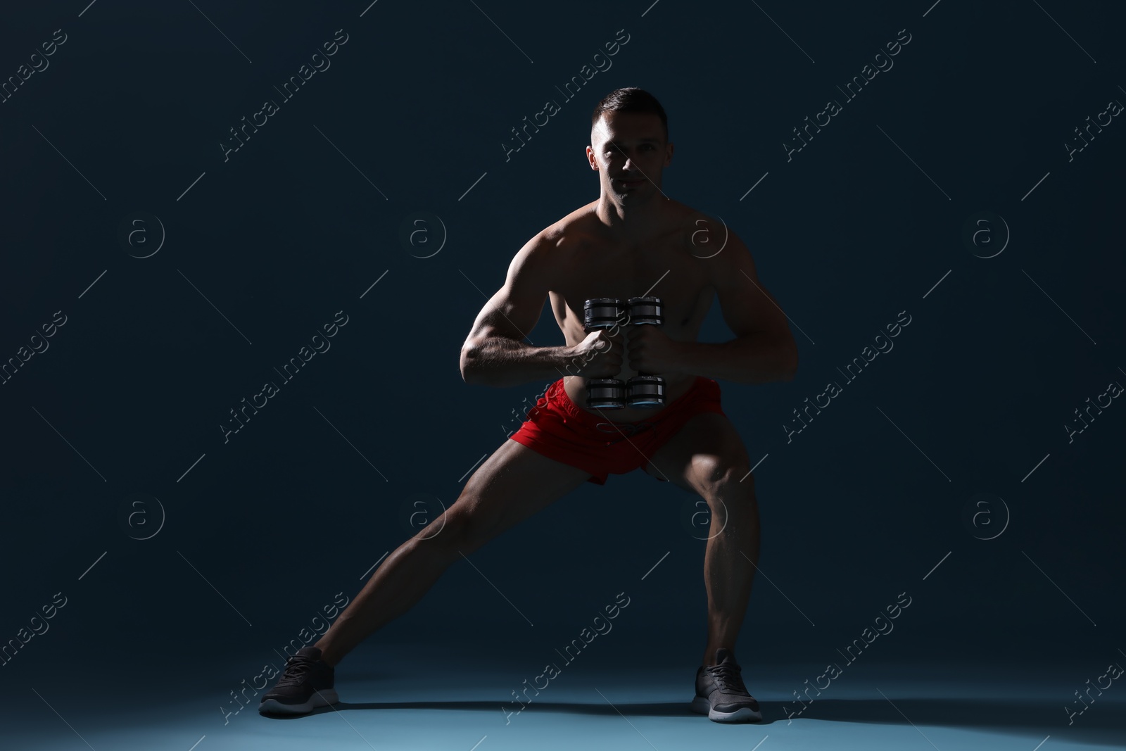 Photo of Man exercising with dumbbells on dark blue background