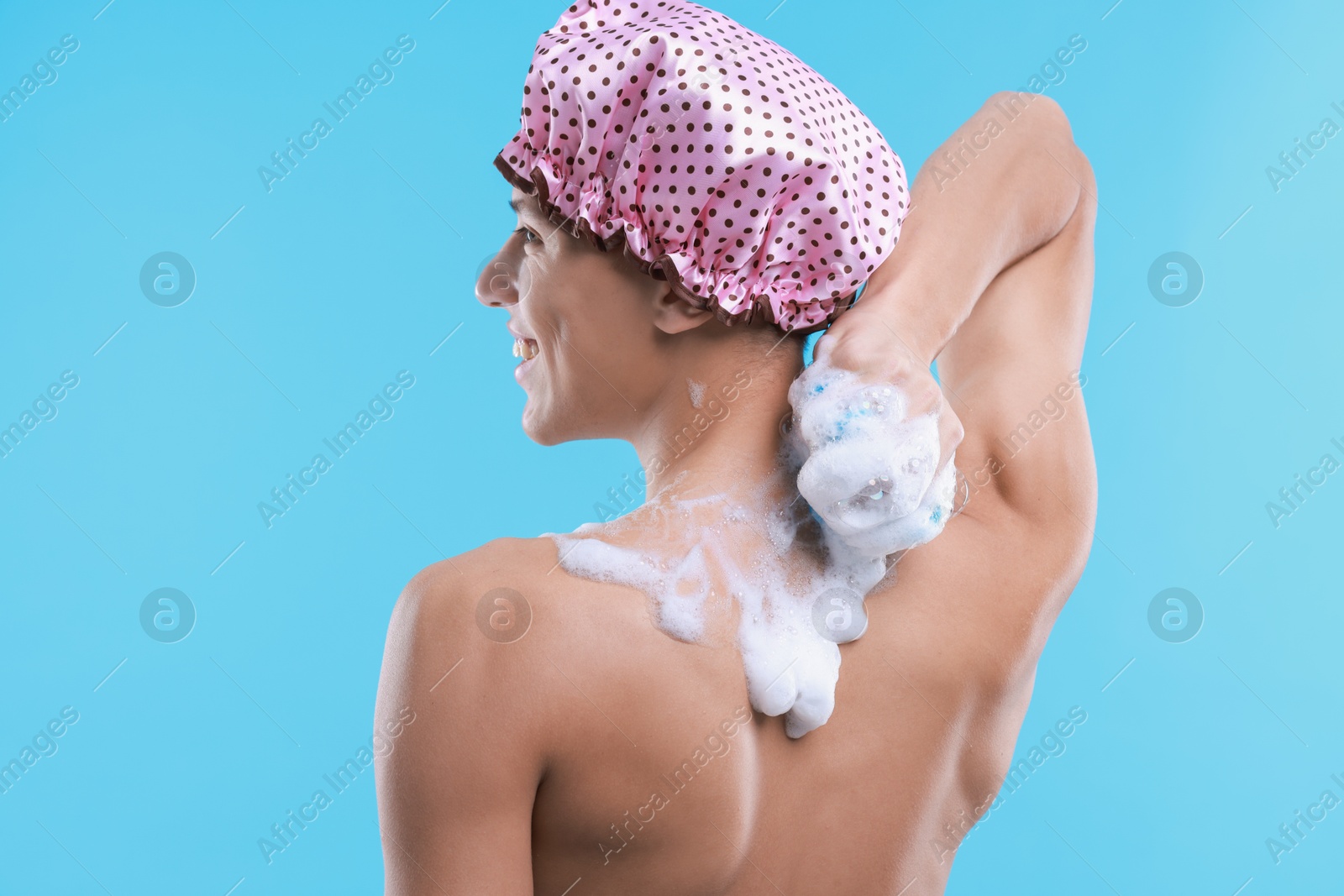 Photo of Man with shower cap and mesh sponge on light blue background