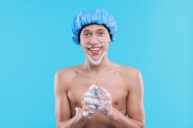 Photo of Man with shower cap and mesh sponge on light blue background