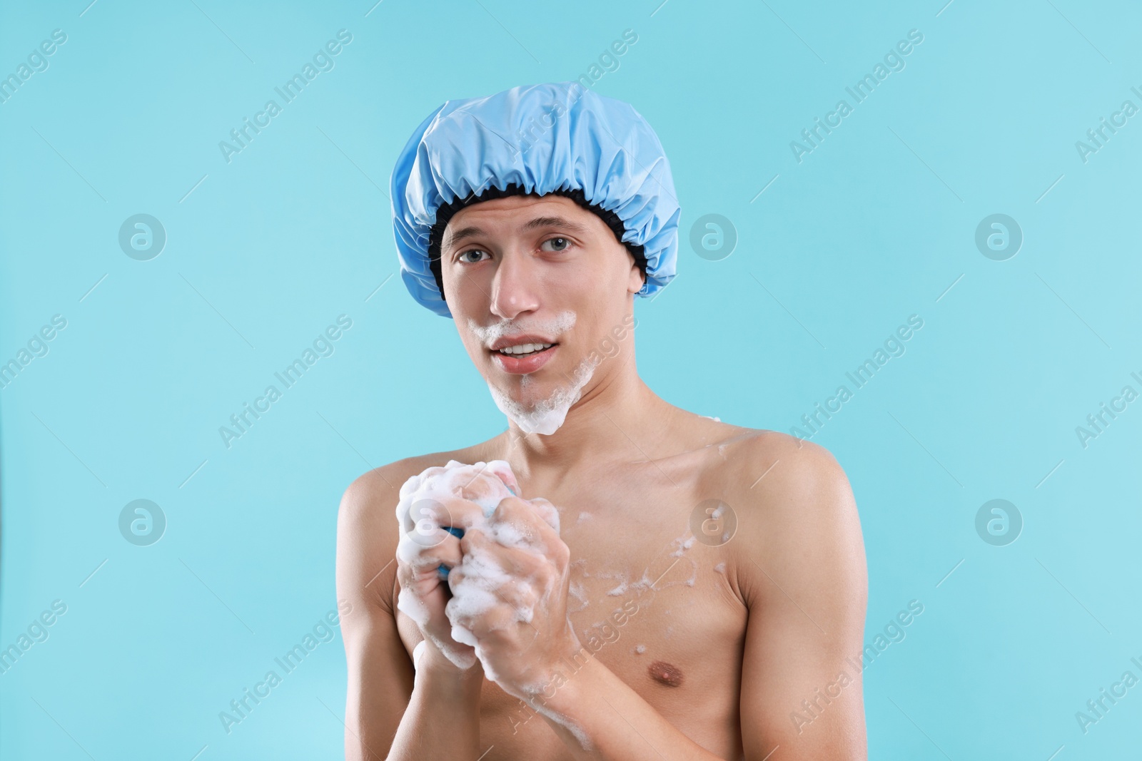 Photo of Man with shower cap and mesh sponge on light blue background