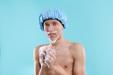 Photo of Man with shower cap and mesh sponge on light blue background