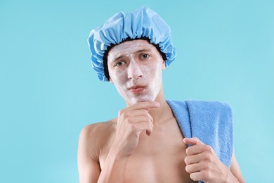 Photo of Man in shower cap with cream on his face against light blue background