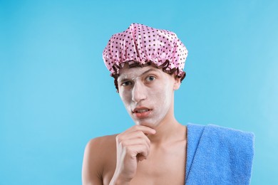 Photo of Man in shower cap with cream on his face against light blue background