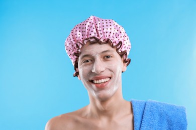 Man in shower cap with cream on his face against light blue background