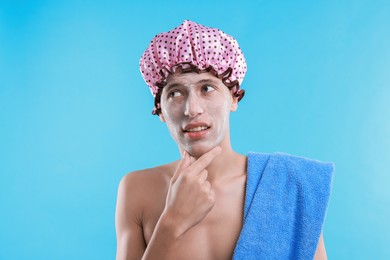 Photo of Man in shower cap with cream on his face against light blue background